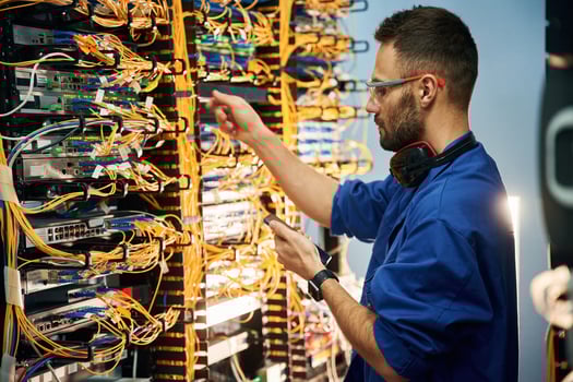 Holding smartphone.., Young man is working with internet equipment and wires in server room photo