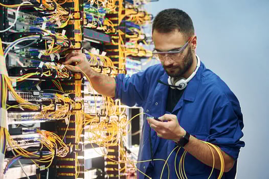 Checking signal, by ,device. Young man is working with internet equipment and wires in server room photo