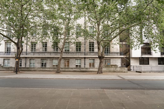 Building with large windows and a clean, modern design, flanked by trees along the sidewalk. The urban scene showcases a quiet street with minimal activity and a clear view of the architecture. photo