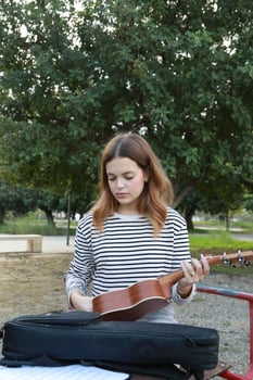 Girl Hand Opens Backpack Bag With Ukulele Instrument Outside In The Outdoor photo