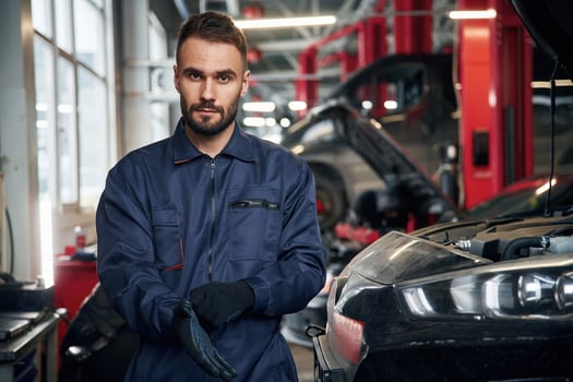 Wearing ,the ,gloves, standing. Car repairman is in the garage with automobile photo