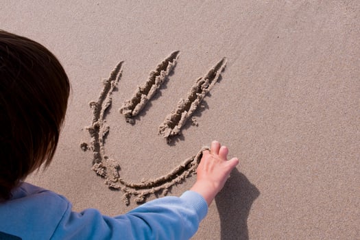 Child drawing smiley face in sand. Fun beach activity photo
