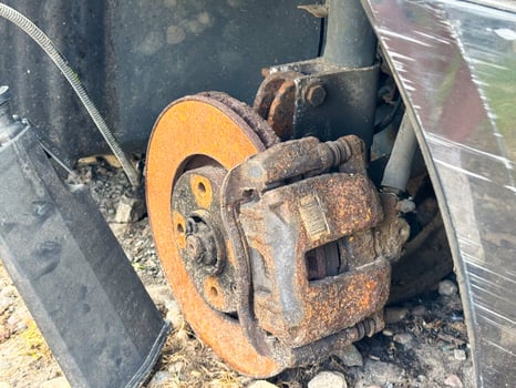 Rusted brake caliper and disc from a car showing severe corrosion on the braking system, with exposed suspension components and wheel hub assembly photo