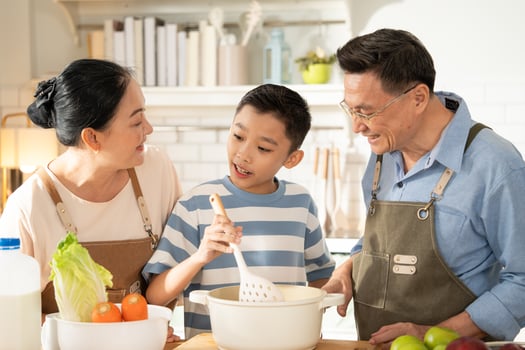 Asian grandparents support and help grandson cooking breakfast in the kitchen. Grandmother and grandfather watching nephew learning skill on morning weekend. Family love and bonding. photo