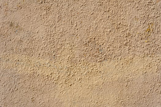 A yellow wall covered with numerous layers of plaster and paint. The layers form small irregularities and bumps. photo