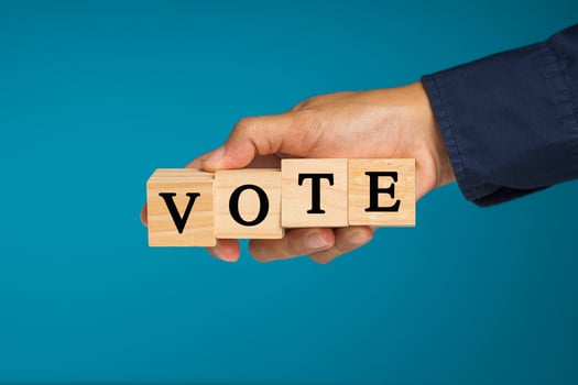 Close-up of hand holding wooden cubes with letters VOTE against a blue background photo