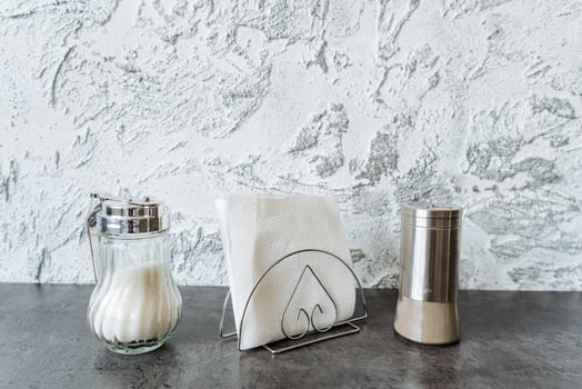 The table elegantly showcases a convenient napkin holder, stylish salt and pepper shakers, and fresh garlic, crafting a casual yet functional atmosphere for dining or meal preparation photo