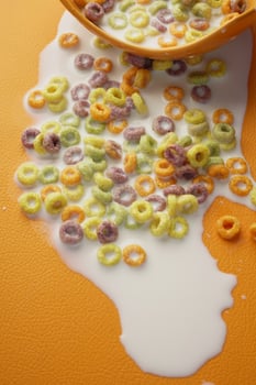 Colorful cereal spills milk on an orange surface in the kitchen photo
