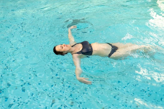 Woman floating calmly in a tranquil swimming pool surrounded by clear blue water photo