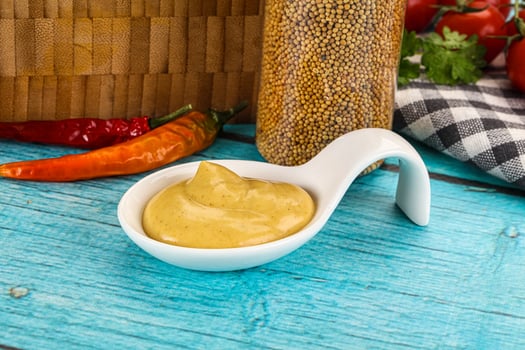 A bowl of mustard and a spoon with chili peppers photo