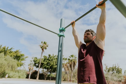 A strong man is hanging from a high bar at an outdoor gym in the Canary Islands, outdoor training photo