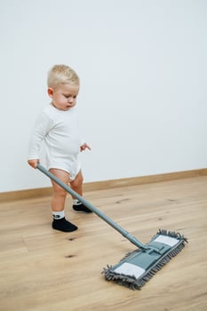 A toddler joyfully cleaning the floor with a mop in a beautifully designed modern home interior photo