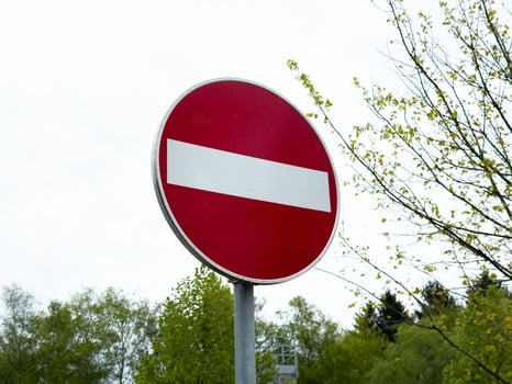 Red and white no entry road sign against tree line and sky background photo