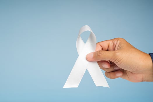 Hand holding a white ribbon symbol the fight lung cancer against on a blue background photo