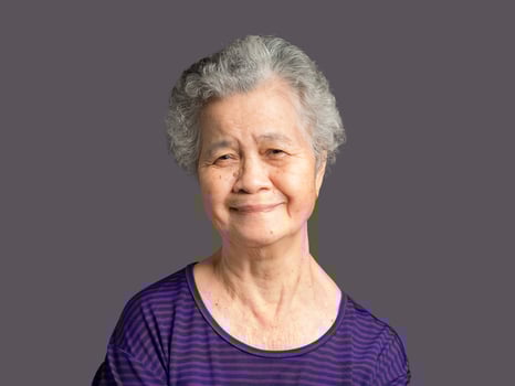 Portrait of an elderly woman looking at the camera with a smile while standing on a gray background. photo