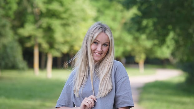 A cheerful young woman with flowing blonde hair is joyfully enjoying a beautiful sunny day in a lovely green park photo