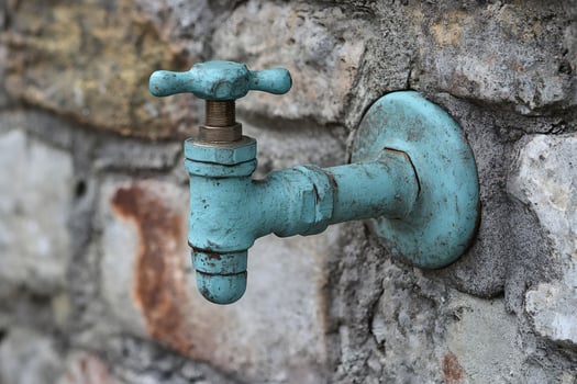 Weathered outdoor faucet against stone wall photo