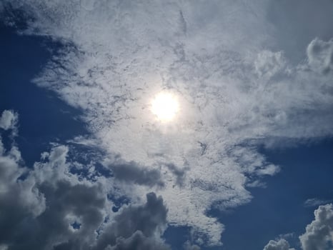 Sun shining through the clouds in a bright blue sky photo