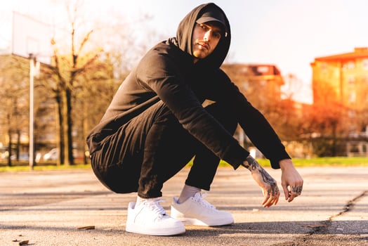 young rapper in black sweatshirt and hoodie posing in the middle of an outdoor basketball court photo