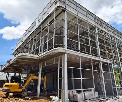A yellow excavator is in front of a building under construction photo