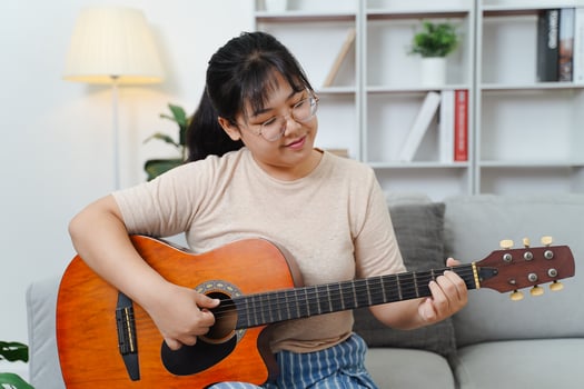 Asian women play acoustic guitar and singing on the sofa in living room at home photo