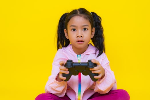 Asian girl playing videogames with joystick on yellow background photo