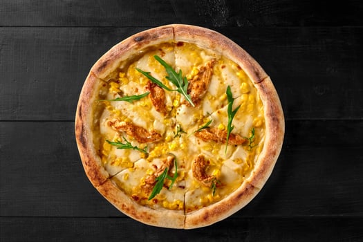 Delicious pizza with chicken, corn, arugula, and cheese on black wooden table photo
