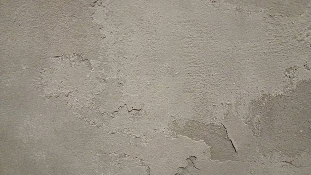 Close-up of a rough, worn-out concrete wall with a gritty texture, featuring cracks and crevices. The color is a dull, muted gray with subtle variations in shade, showing off the uneven surface. photo