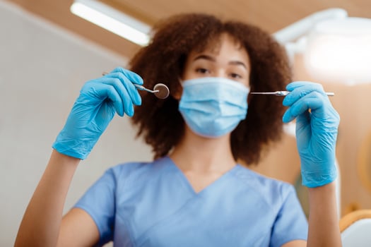 Portrait of young dentist in modern clinic. African american female in uniform, protective mask and gloves holds medical instruments for examination of patient, bottom view, close up, free space photo