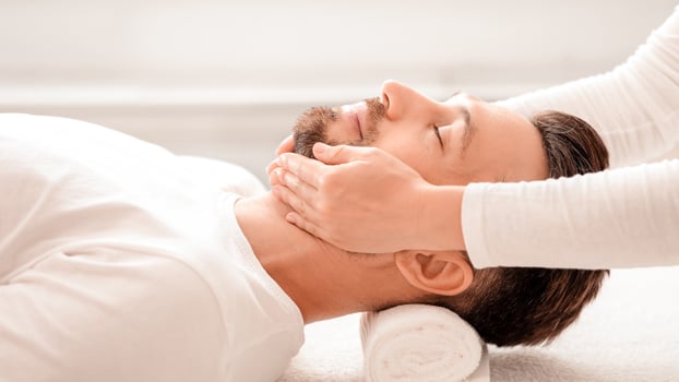 Middle aged man attending spa salon, getting anti-aging face massage, side view. Unrecognizable cosmetologist massaging relaxed bearded man chin, making lifting procedures. Male cosmetology concept photo
