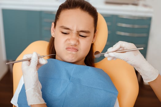 Distrust of dentist and dental treatment. Portrait of small hispanic kid in chair looking at hands of doctor in rubber gloves with medical instruments in modern clinic interior, pov, free space photo