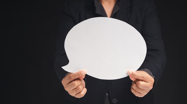 Close-up of a businessman holding a blank white speech bubble while standing on a black background. Space for text. photo