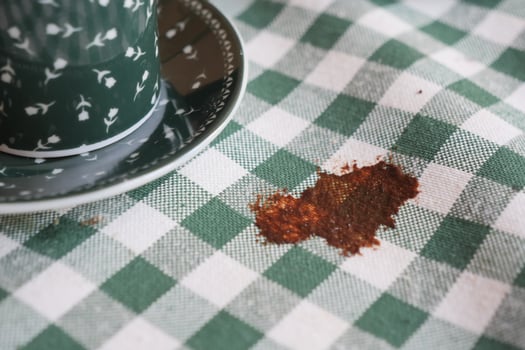 Coffee spill on a green checkered tablecloth with a cup nearby photo