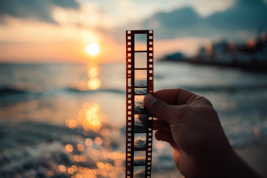 Close-up of hand holding vintage film strip in front of sunset over sea photo
