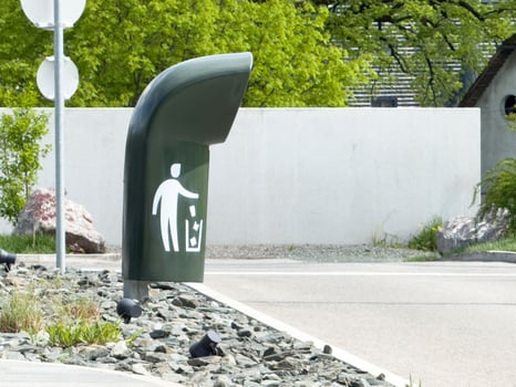 Unique modern trash can on street corner with icon for litter disposal and greenery in background photo