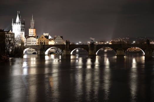A beautiful bridge over a river at night, with a lit city behind photo