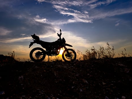 Silhouette of Motorcycle Against Dramatic Sunset Sky with Grassy Hill and Clouds in the Background photo