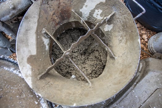 View of a concrete mixer drum showing wet concrete, aggregate, and metal crossbars. Construction materials like gravel and a black plastic bag are nearby. photo