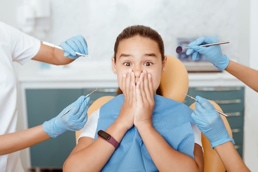 Fear of dental treatment and ortodont. Horror emotions on face of little girl, covering her mouth with hands, doctors hands in rubber gloves holds medical instruments in modern clinic, cropped photo