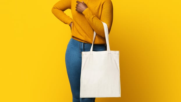 Mockup For Design. Cheerful African American Lady Holding Blank White Eco Tote Canvas Bag With Copy Space, Positive Black Female Posing Over Yellow Background In Studio, Smiling At Camera photo