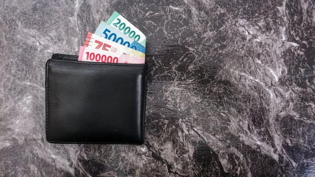 Yogyakarta, Indonesia, 2025 - Black wallet with several Indonesian Rupiah banknotes with different values in it isolated on pattern background photo