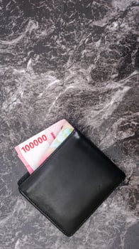 Yogyakarta, Indonesia, 2025 - Black wallet with several Indonesian Rupiah banknotes in it isolated on pattern background photo