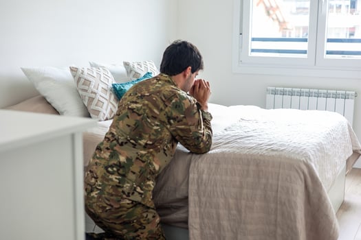 Depressed soldier kneeling and praying by his bed at home photo