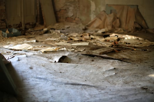 Damaged bulging floor covered in torn paper, dust, and debris inside an abandoned and neglected room photo