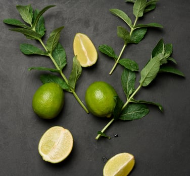 Whole and cut limes with fresh mint leaves arranged on a dark textured surface. Composition perfect for food, drink, or summer themes photo