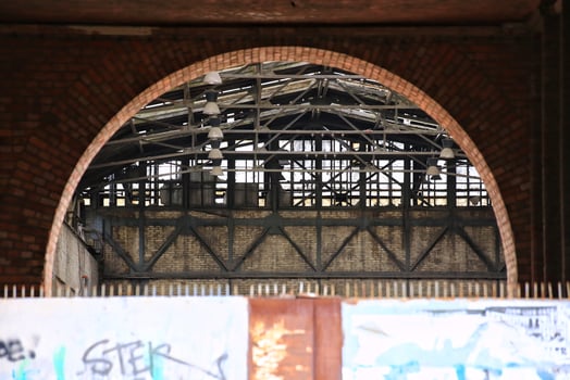 Brick arch behind steel gate framing an abandoned industrial building with exposed beams and hanging lights photo