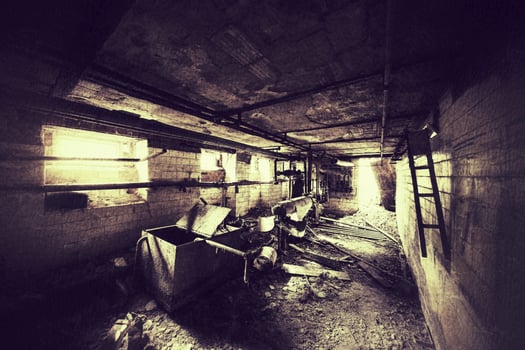 Dark abandoned basement with rusted pipes, broken equipment, and scattered debris on the floor photo