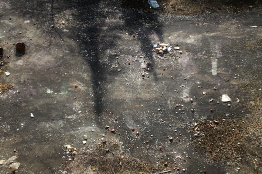 Shadowed concrete ground with scattered rubble, dry brush, and faint surface markings photo