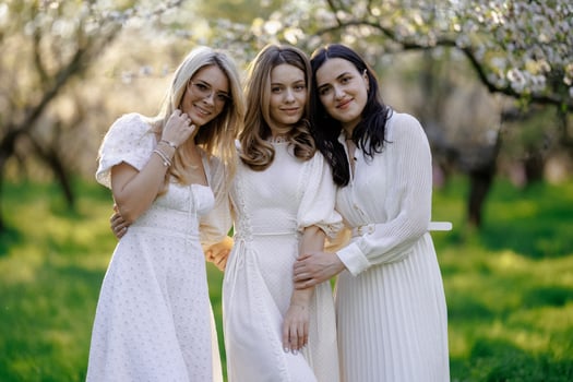 Three women in white dresses are happily posing in a park photo