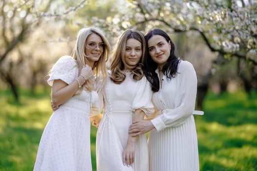 Three women pose elegantly in white dresses for a park photo